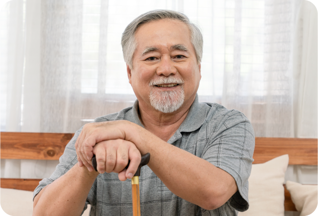 Older man sitting and holding a cane.
